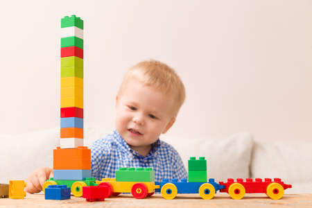 Portrait of child playing with colorful plastic bricks at the table. Toddler having fun and building a train out of constructor bricks. Early learning. Developing toysの写真素材