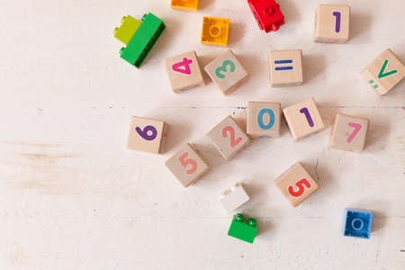 Top view on wooden cubes with numbers and colorful plastic bricks on white wooden table background. School, education and learning concept.の写真素材