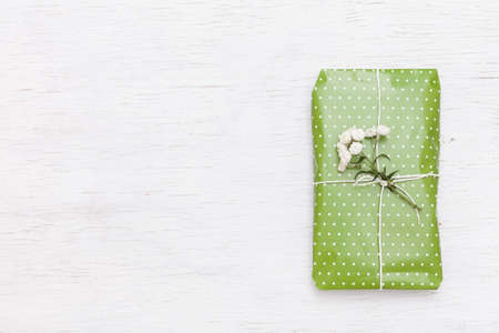 Top view on nice wrapped gift with flowers on white wooden background. Present for birthday, Christmas and any other celebration. Holidays conceptの写真素材
