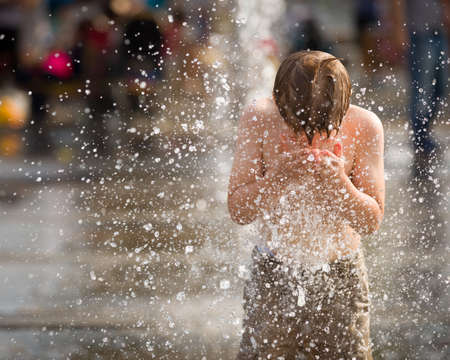 Portrait of cute kid boy playing with fountain on the street on a sunny day. Child having fun outdoors.の写真素材