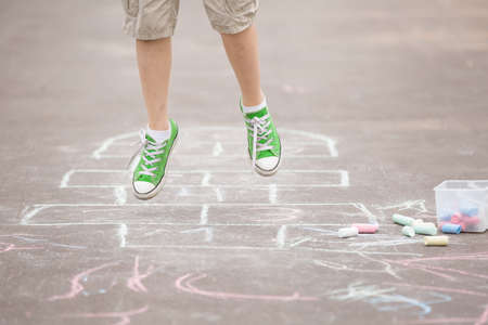 Closeup of boy's legs and hopscotch drawn on asphalt. Child playing hopscotch on playground outdoors...