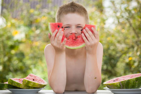 Happy cute child eating big red slice of sweet watermelon in the garden. Kid boy enjoying delicious watermelon on sunny summer day. Healthy food and lifestyle conceptsの写真素材