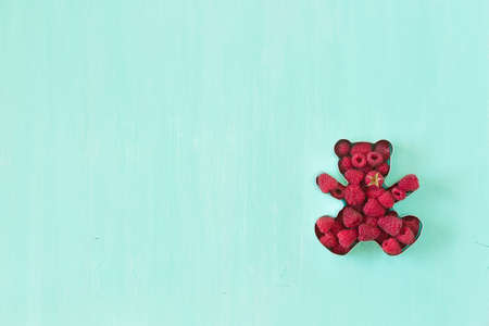 Teddy bear shaped mold for the cookies full of fresh organic raspberries on turquoise background.の写真素材