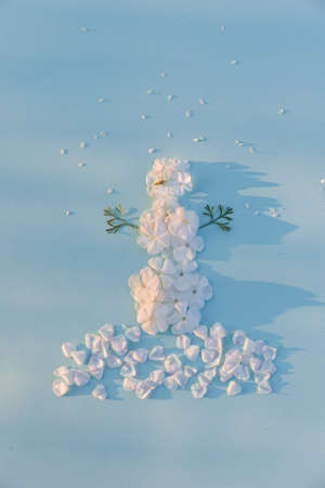 Top view on funny snowman made of white flowers petals on light blue background with sun shine. Holidays, winter and Christmas conceptの写真素材