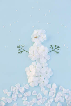 Funny snowman made of white flowers petals on light blue background. Christmas, holidays and winter concept.の写真素材