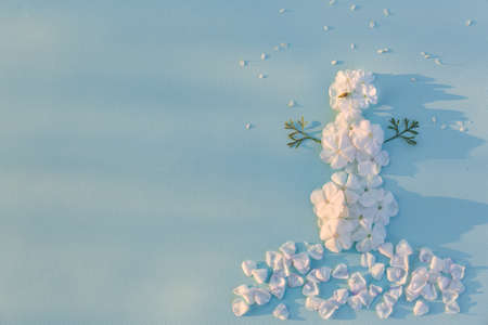 Top view on funny snowman made of white flowers petals on light blue background with sun shine. Holidays, winter and Christmas conceptの写真素材