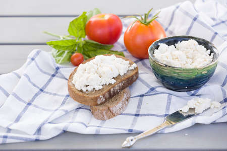 Organic Farming Cottage cheese in a green bowl, slice of whole wheat bread with Homemade Ricotta cheese served with tomatoes and basil on wooden board  on linen fabric. Healthy food conceptの写真素材