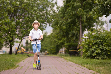 Cute kid boy riding his scooter and having fun in the park on a sunny day. Activities with children outdoors. Child on scooter. Lifestyle and active leisure concept.の写真素材