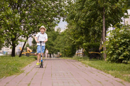Cute kid boy riding his scooter and having fun in the park on a sunny day. Activities with children outdoors. Child on scooter. Lifestyle and active leisure concept.の写真素材