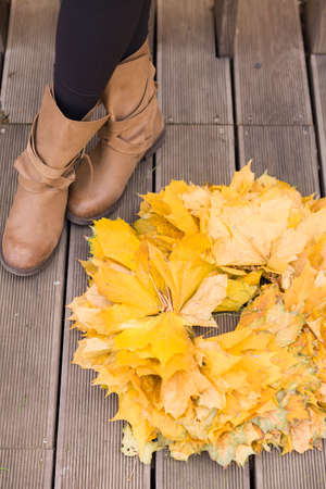Top view on beautiful yellow maple wreath and womans feet on wooden background. Girl with autumn...