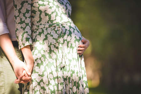 Closeup of tummy of a pregnant woman. Man hugging his pregnant wife in a sunny day. Torso of young pregnant woman caressing her belly. Future mom expecting baby. Maternity, family and new life conceptの写真素材