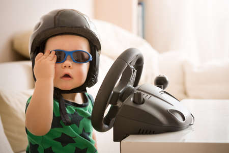 Cute little kid boy in a helmet playing with Computer steering wheel. Future driver. Getting ready...