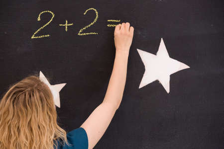 Young girl drawing question mark on a black background. woman drawing question mark for the math task on the board. Teacher hand drawing question mark on chalkboard. Education, back to school conceptの写真素材