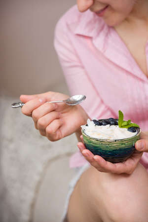 Closeup of woman's hands holding cup with organic yogurt with blueberries, coconut and fresh mint. Homemade vanilla yogurt in girl's hands. Breakfast, snack. Healthy eating and lifestyle conceptの写真素材