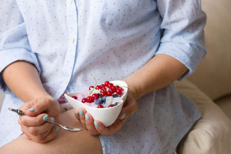 Closeup of woman's hands holding cup with organic yogurt with blueberries, coconut and fresh mint. Homemade vanilla yogurt in girl's hands. Breakfast, snack. Healthy eating and lifestyle conceptの写真素材