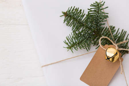 Christmas gift box with tag. New Year present in white box with fir branches at white wooden table. Flat lay with copy space. Celebration, holiday season and winter conceptの写真素材