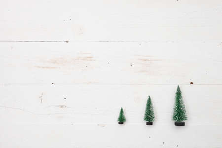 Top view on three little Christmas trees on white wooden background. Holidays and winter concept.の写真素材