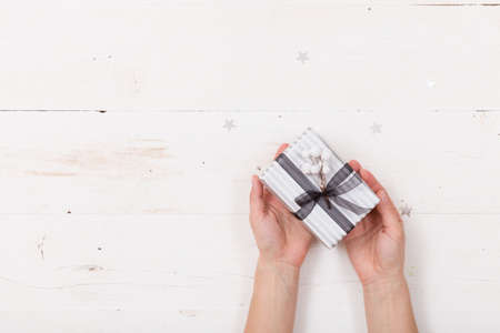 Top view on woman's hands holding nice Christmas gift packed in striped paper with ribbon. Present. Celebration and holiday seasonの写真素材
