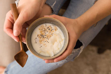 Closeup of woman's hands holding cup with organic yogurt with coconut and chia seeds. Homemade vanilla yogurt in girl's hands. Breakfast, snack. Healthy eating and lifestyle conceptの写真素材