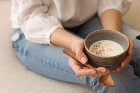 Closeup of woman's hands holding cup with organic yogurt with coconut and chia seeds. Homemade vanilla yogurt in girl's hands. Breakfast, snack. Healthy eating and lifestyle conceptの写真素材
