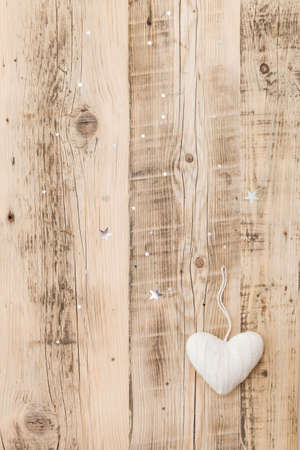 Knitted white heart Christmas decoration on retro wooden background with sparkling stars. Holiday season and celebration concept.の写真素材