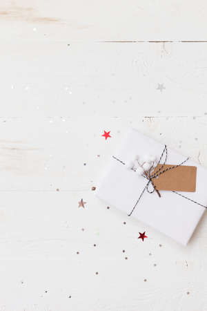 Top view on nice Christmas gift wrapped in white gift paper, Christmas tree decorations on white wooden background with sparkling stars. New Year, holidays and celebration conceptの写真素材