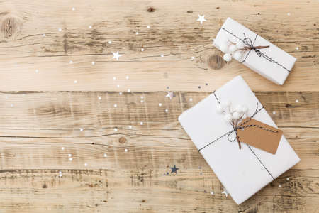 Top view on nice Christmas gift wrapped in white gift paper on wooden background with sparkling stars. New Year, holidays and celebration conceptの写真素材