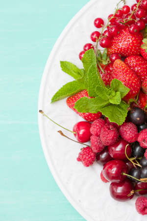 Closeup of white plate full of fresh organic berries: strawberries, blueberries, raspberries, gooseberry, blackcurrant decorated with mint as summer dessert or snack. Healthy food and eating conceptの写真素材