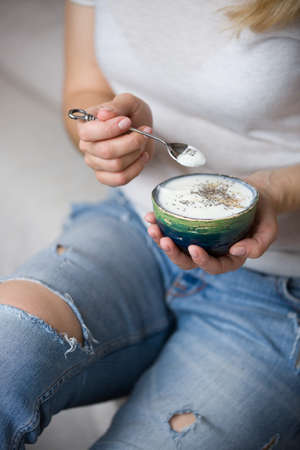 Closeup of woman's hands holding cup with organic yogurt with blueberries, coconut and fresh mint. Homemade vanilla yogurt in girl's hands. Breakfast, snack. Healthy eating and lifestyle conceptの写真素材