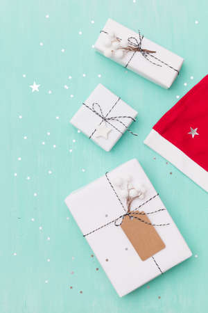 Top view on nice Christmas gifts wrapped in white gift paper, Christmas tree decorations,  Santa's hat on wooden background with sparkling stars. New Year, holidays and celebration conceptの写真素材