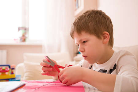 Cute kid boy crafting with scissors and color paper at his desk. Hobby, activities for children. School child making some crafts.の写真素材