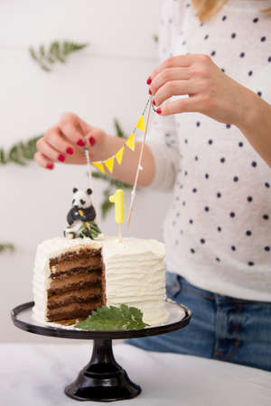 Closeup of woman's hands taking out birthday cake decorations. Celebration treats. Healthy carrot cake for 1 year old baby decorated with toy panda and flags banner.の写真素材