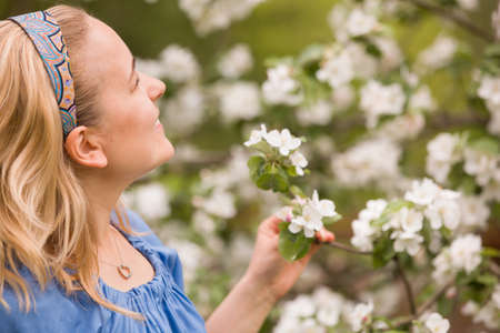 Portrait of a young smiling woman looking at apple trees' flowers. Girl and blooming apple tree. Spring time with trees flowers.の写真素材
