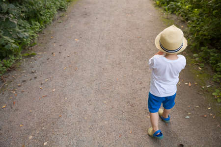 Top view on cite little toddler boy in straw hat walking on the countryside road on sunset. Lifestyle conceptの写真素材