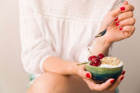 Closeup of woman's hands holding a cup with organic yogurt with oats and cherries. Homemade vanilla yogurt in girl's hands. Breakfast or snack. Healthy eating and lifestyle concept.の写真素材