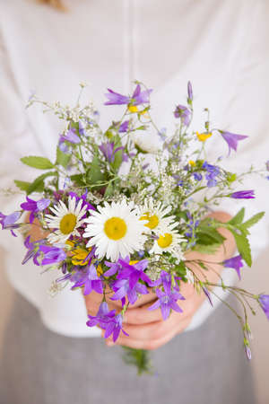Closeup of woman's hands holding beautiful bunch of wild flowers. Girl with summer bouquet at white wallの写真素材