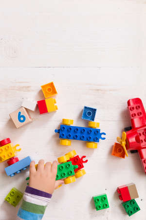 Child playing with wooden cubes with numbers and colorful toy bricks on a white wooden background. Toddler learning numbers. Hand of a child taking toysの写真素材