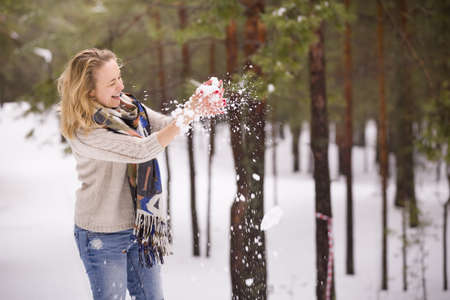 Snow in hands of a young blond woman with red manicure, warm sweater and yellow scarf. Winter walks outdoors. Snow in the forest.の写真素材