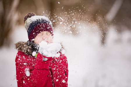 Portrait of cute kid boy blowing snow from his hands on a winter day. Child playing outdoors. Lifestyle conceptの写真素材
