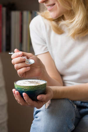 Closeup of woman's hands holding cup with homemade organic vanilla yogurt with chia seeds....