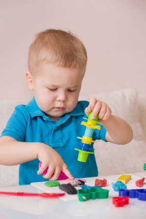 Child with colorful clay. Toddler playing and creating toys from play dough. Boy molding modeling...
