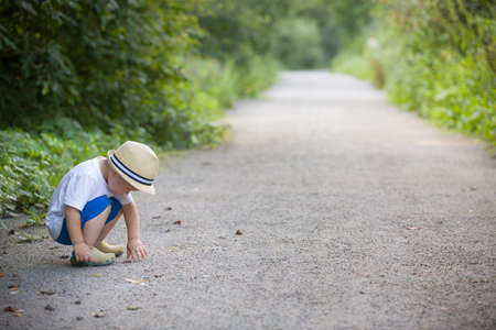 Cute little toddler boy in straw hat palying on the countryside road on a sunny summer day. Lifestyle conceptの写真素材