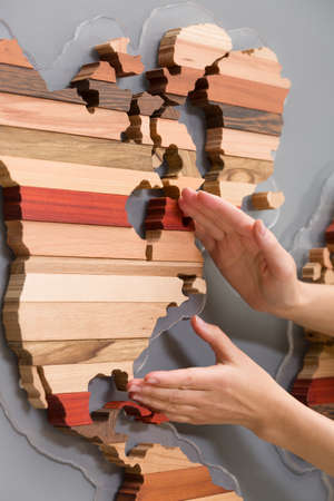 Woman's hands holding handmade wooden map for home decoration. Art and abstract. Different types of wood in shape or continents on light grey background.の写真素材