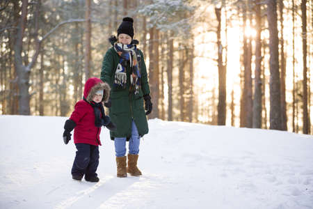 Mother and little toddler boy walking in the winter forest and having fun with snow. Family enjoying winter. Child and woman watching falling snow outdoors. Winter, Christmas and lifestyle concept.の写真素材