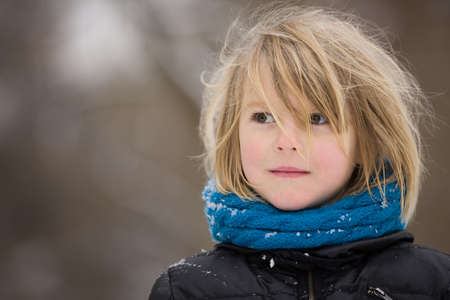 Portrait of adorable little kid boy with long blond hair outdoors. Child with blue scarf walking on a windy dayの写真素材