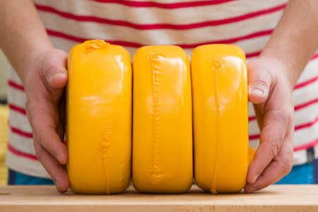 Three big organic cheese heads in yellow vacuum package in man's hands. Food conceptの写真素材