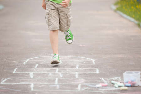 Closeup of boy's legs and hopscotch drawn on asphalt. Child playing hopscotch on playground outdoors...