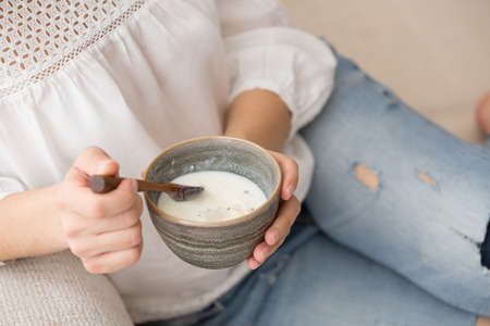 Closeup of woman's hands holding cup with organic yogurt with coconut and chia seeds. Homemade vanilla yogurt in girl's hands. Breakfast, snack. Healthy eating and lifestyle conceptの写真素材