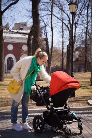 Young happy woman walking with stroller in the city. Mother with baby child in a pram. Lifestyle conceptの写真素材