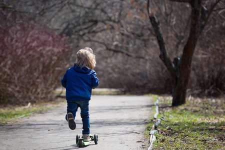 Cute kid boy riding his scooter and having fun in the park on a sunny day. Activities with children...